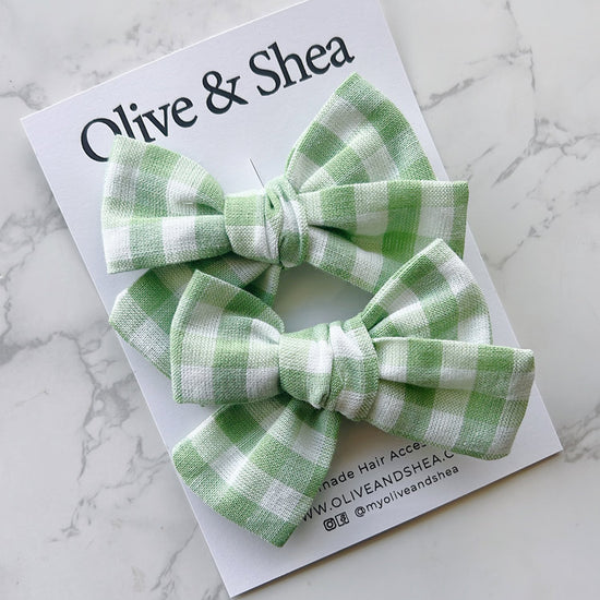 Green gingham hair bows on a white card with 'Olive & Shea' branding on a marble background.