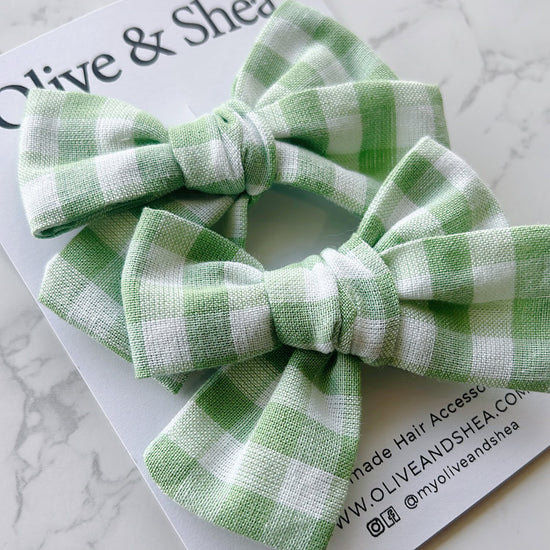Green checkered hair accessories on a marble surface with Olive & Shea branding.