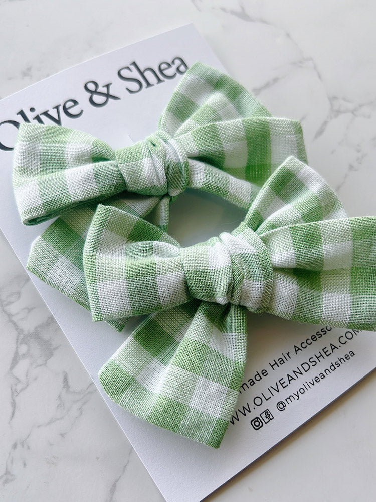 Green checkered hair accessories on a marble surface with Olive & Shea branding.