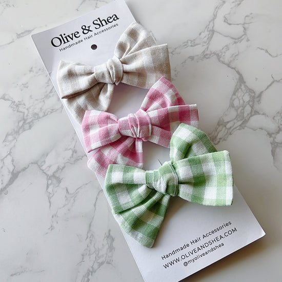 A set of three hand tied bows in beige, pink, and green on a marble surface