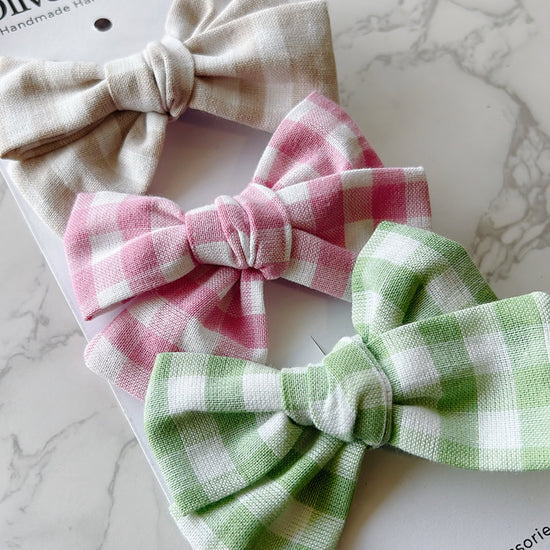 Three hand tied bows in beige, pink, and green on a marble surface