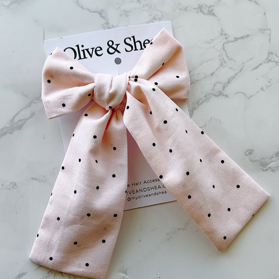 Pink polka dot hair bow on a marble surface with a brand card.