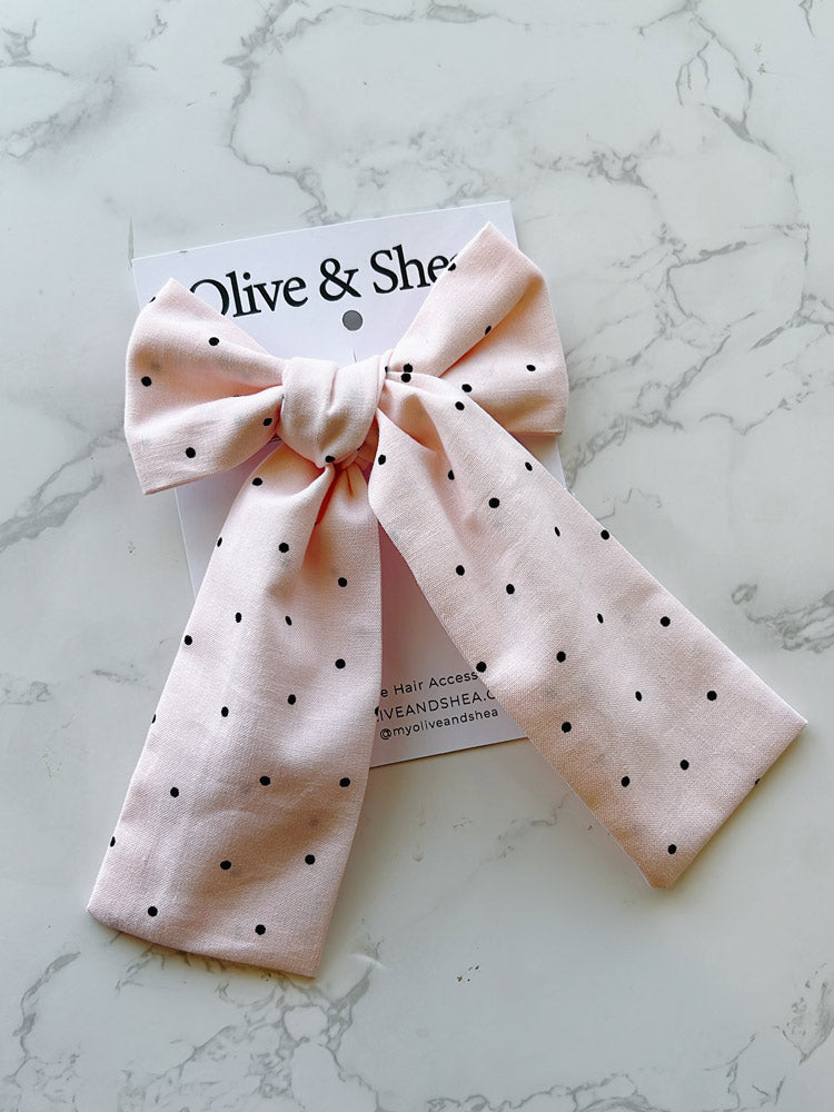 Pink polka dot hair bow on a marble surface with a brand card.
