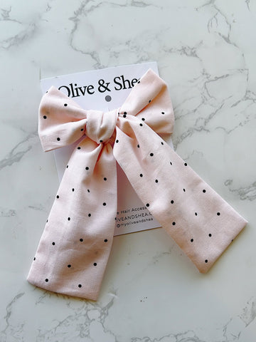 Pink polka dot hair bow on a marble surface with a brand card.