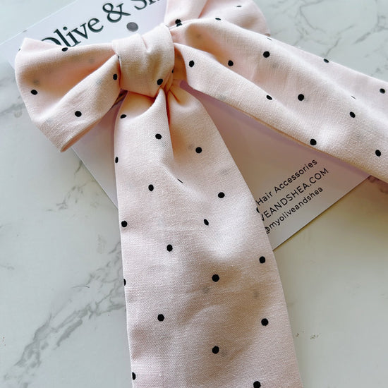 Pink polka dot hair bow on a marble surface with a brand card.