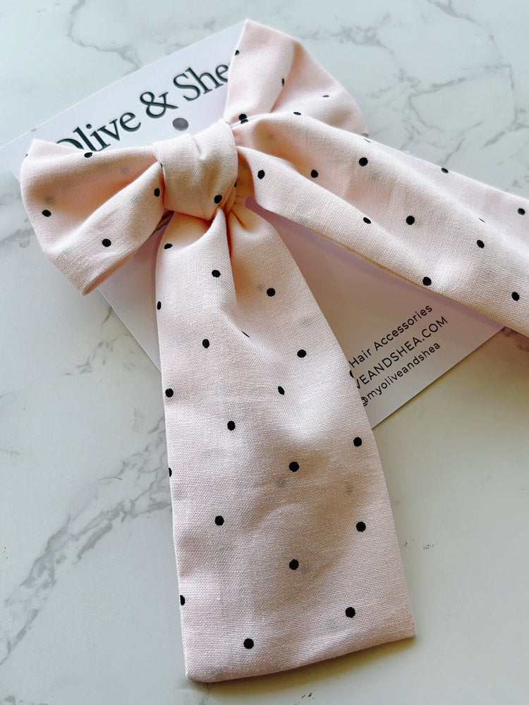 Pink polka dot hair bow on a marble surface with a brand card.